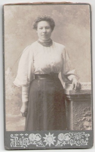 Portret kobiety, włosy upięte, czerwone korale, stojący Fotografia na kartoniku firmowym Odessa [ca 1900]