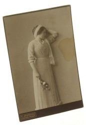Portret młodej kobiety, stojący, przepaska na głowie, kwiaty w dłoni Fotografia na tekturce firmowej / albumin (Poznań ca 1900 K. Ignatowicz)
