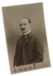 Portret mężczyzny, półpostać, podkręcony wąs, fryzura z przedziałkiem, gładkie uczesanie Fotografia na tekturce firmowej / odbitka srebrowożelatynowa (Bad-Oeynhausen 1906 C. Colberg)