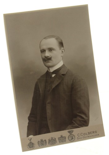 Portret mężczyzny, półpostać, podkręcony wąs, fryzura z przedziałkiem, gładkie uczesanie Fotografia na tekturce firmowej / odbitka srebrowożelatynowa (Bad-Oeynhausen 1906 C. Colberg)