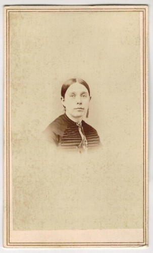 ​Portret kobiety - popiersie, brosza, kolczyki, włosy gładko zaczesane Fotografia na kartoniku firmowym ca. 1900 / USA