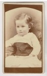 ​Portret dziewczynki - siedzący, biała sukienka, krótkie włosy Fotografia na kartoniku firmowym ca. 1900 / USA