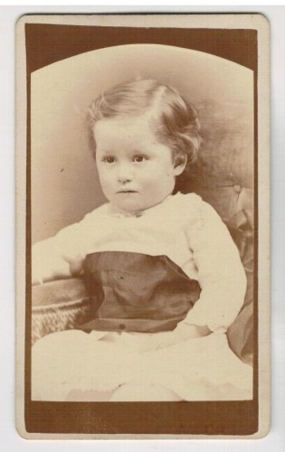 ​Portret dziewczynki - siedzący, biała sukienka, krótkie włosy Fotografia na kartoniku firmowym ca. 1900 / USA