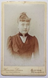 Portret młodej kobiety - popiersie, brosza, włosy upięte, grzywka Fotografia na kartoniku firmowym ca. 1900 / Niemcy